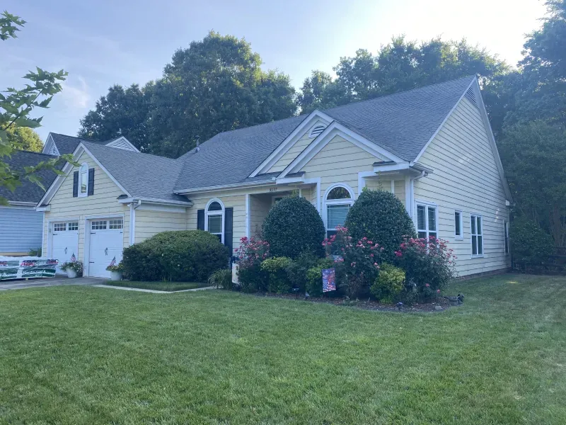Yellow house with a two-car garage, black shutters, and well-maintained landscaping.