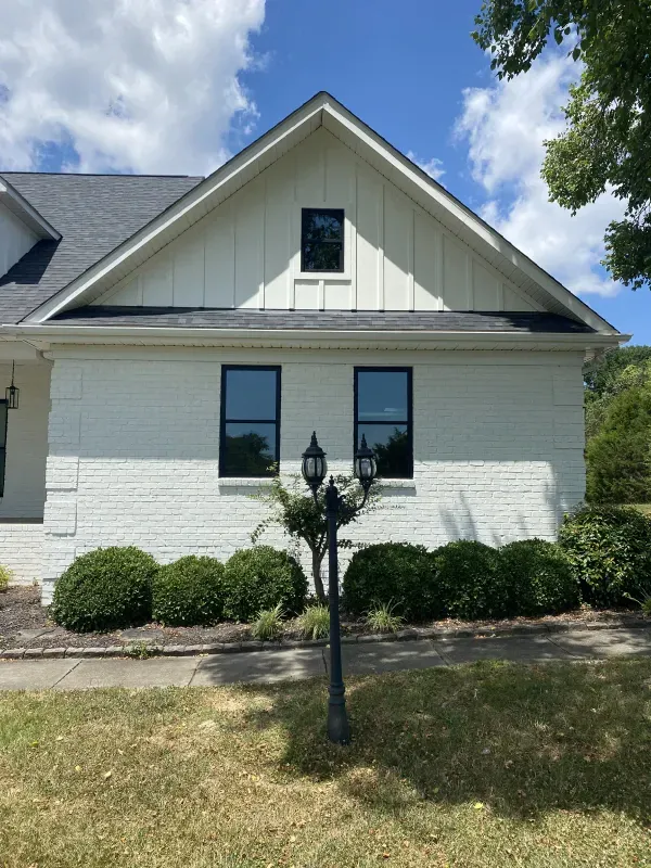 White brick house with black-framed windows and a small gable window under a dark roof.