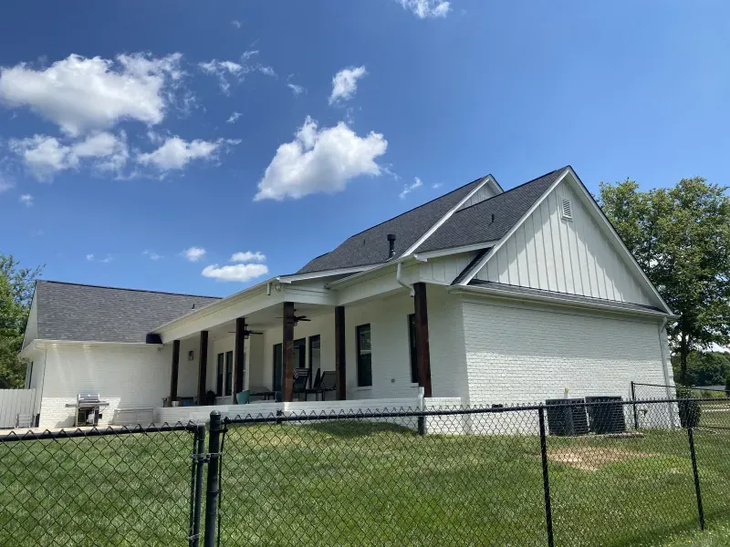 White house with dark roof and trim, green lawn, blue sky with clouds.