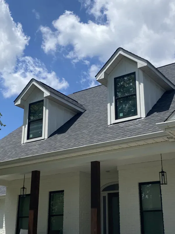 White house with dark roof and two dormer windows under a blue sky.