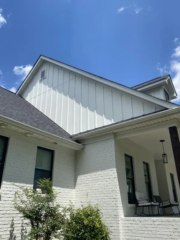 White house with vertical siding and brick, under a blue sky.