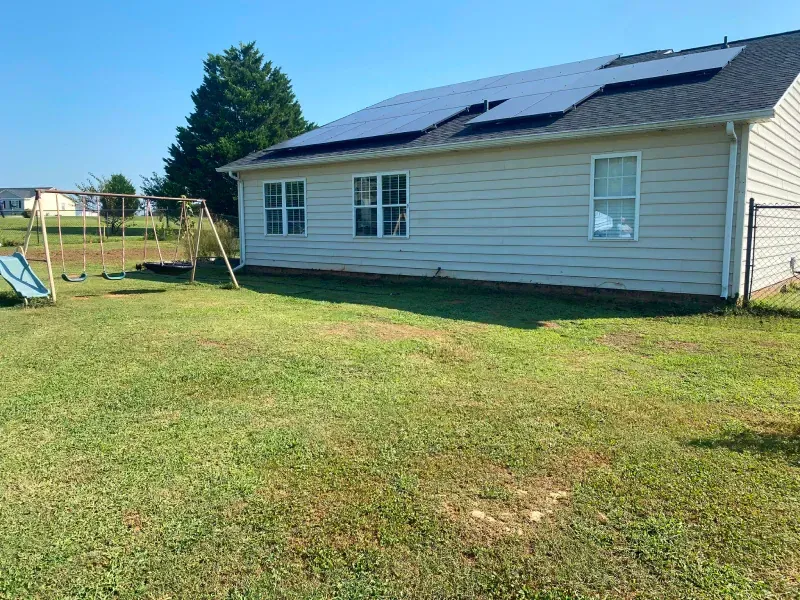 Backyard with a house, solar panels on the roof, and a swing set on a sunny day.