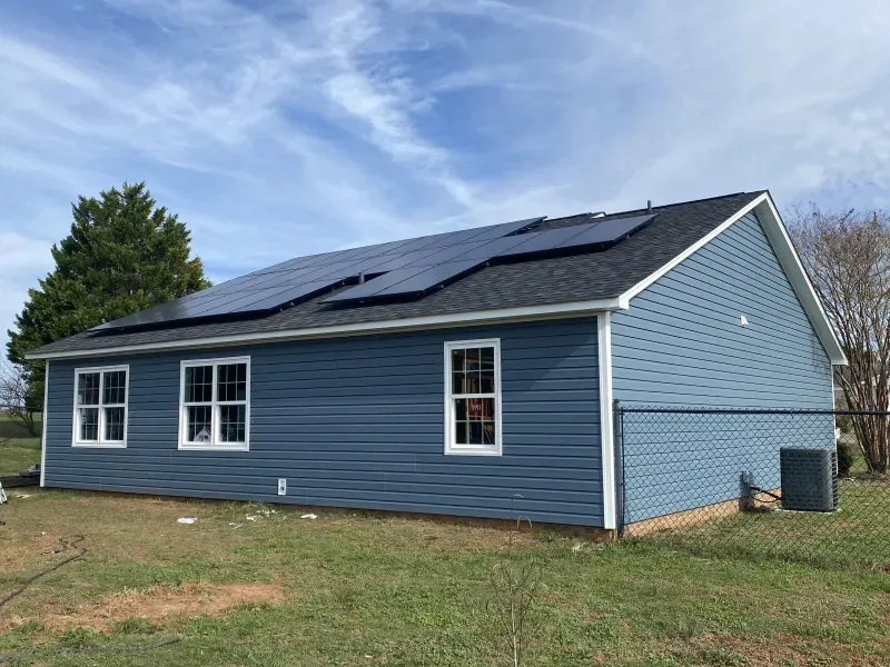 Blue house with solar panels on roof, white window trim, and a cloudy sky.