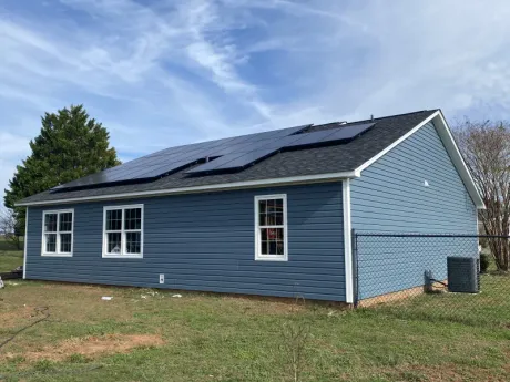 Blue house with solar panels on roof, white window trim, and a cloudy sky.