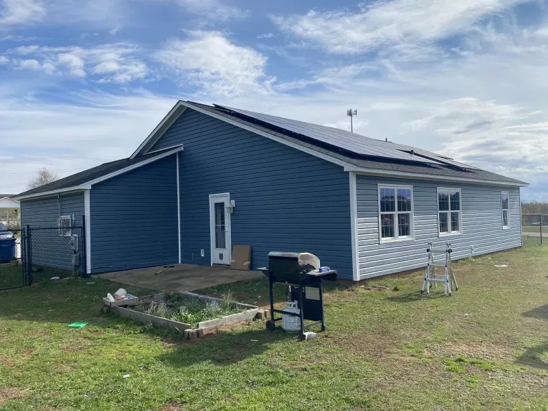 A blue house with solar panels on the roof and a backyard with a grill and garden.