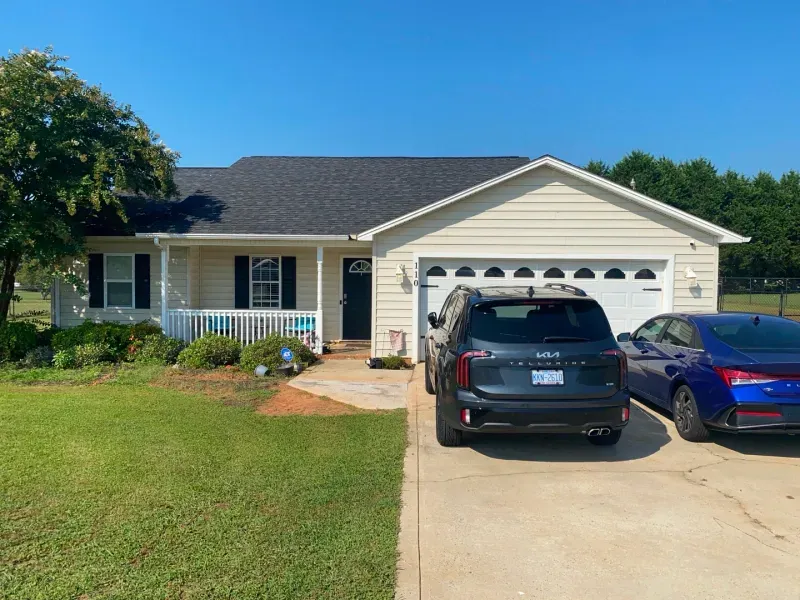 Beige house with two cars parked in the driveway; a Kia Telluride and a blue sedan.