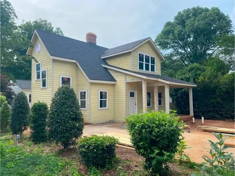 Yellow two-story house with black roof, covered porch, and small bushes in front.