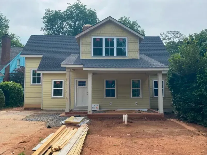 Yellow house under construction with white trim, gray roof, porch, and exposed dirt.