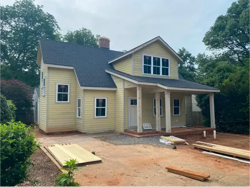 Yellow house under construction with porch, windows, and dark roof.