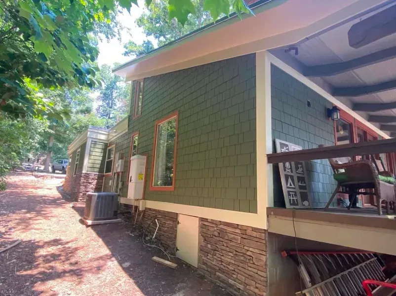 Green shingled house exterior with brown stone foundation, beige trim, and a porch on the right.