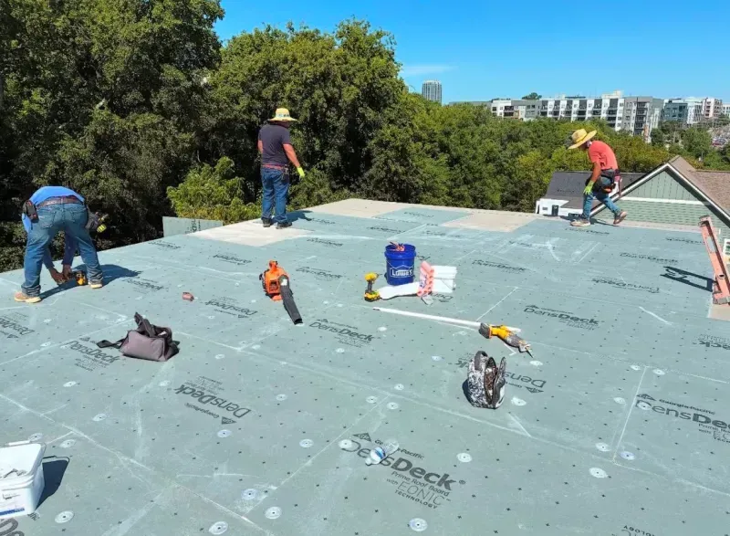 Roofers working on a residential roof, installing underlayment on a sunny day.