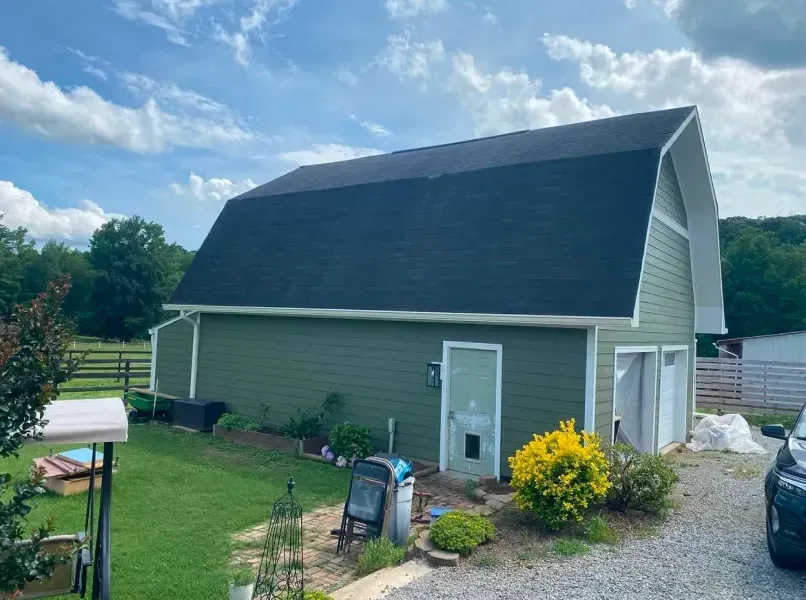 Green barn with black roof and white trim under a blue sky.