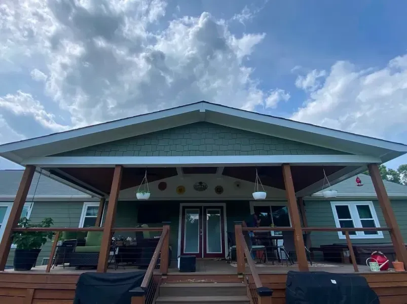 Wooden deck with green house, covered porch and cloudy sky.