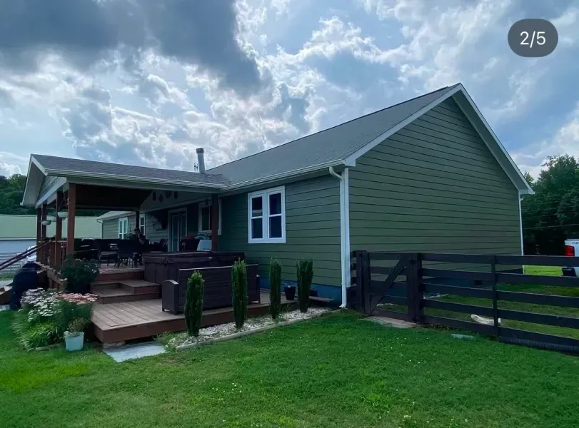 Green house with a wooden deck, black fence, and cloudy sky.