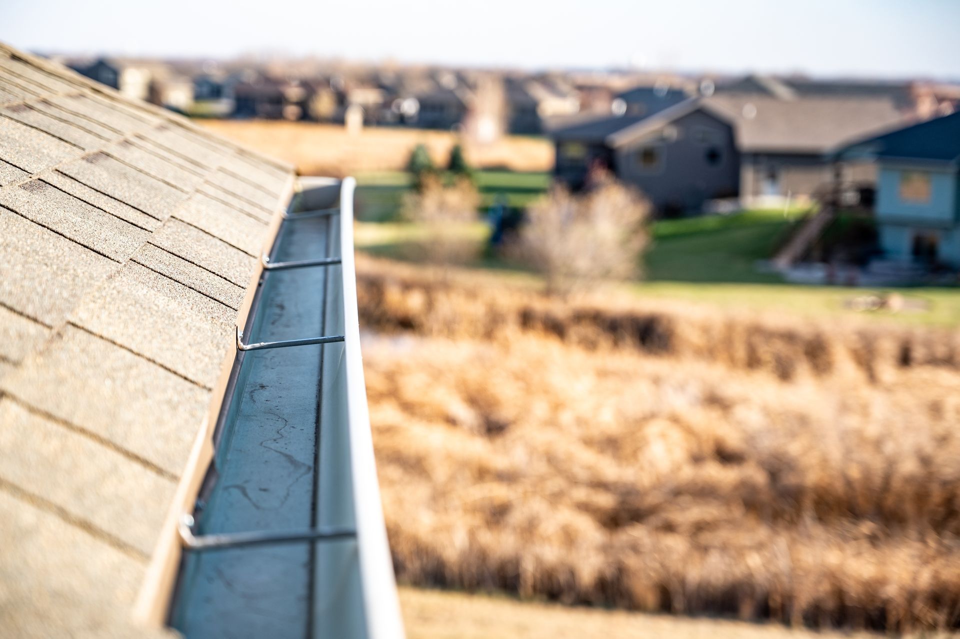 Gutter on a roof with a residential neighborhood in the blurred background.