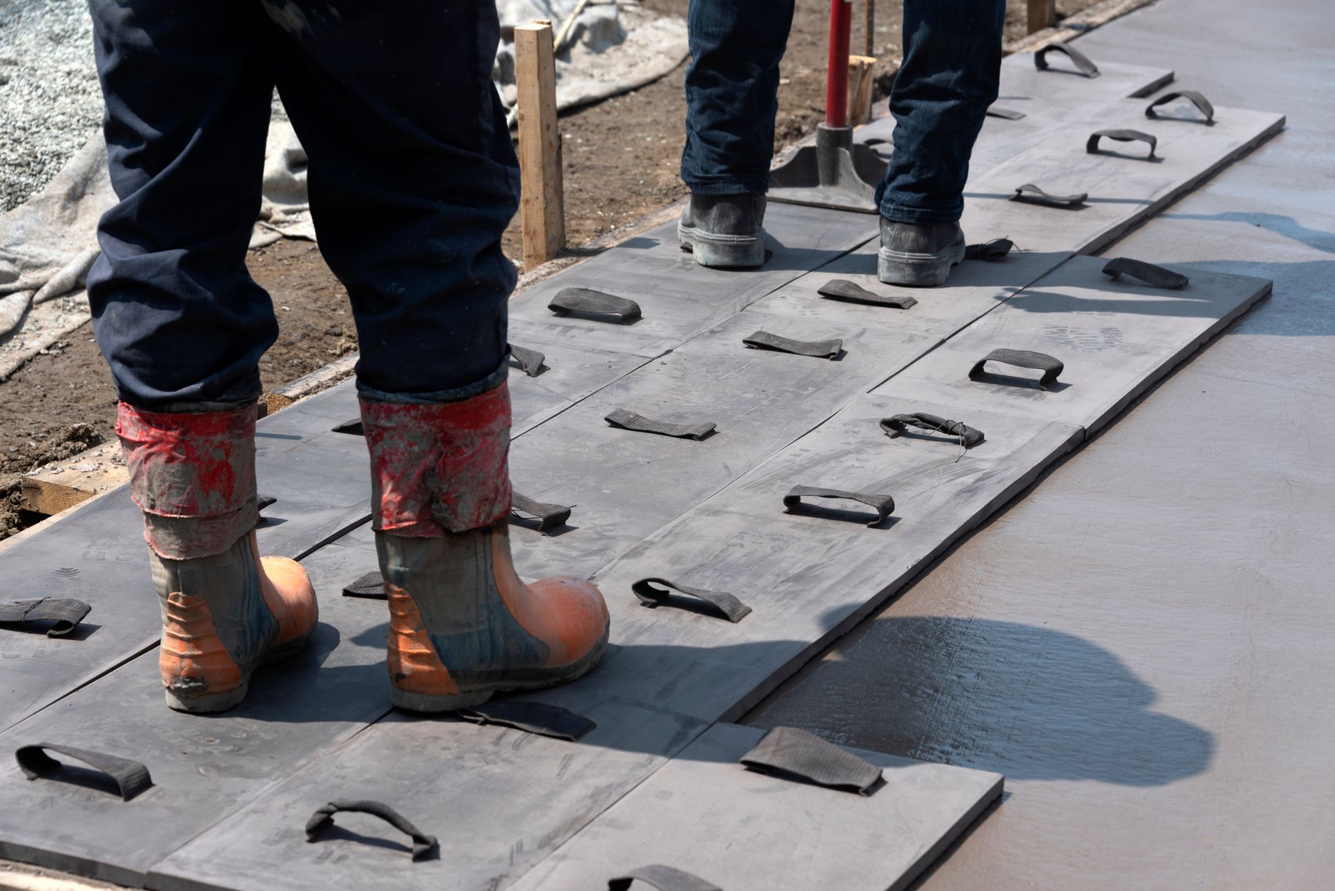 Workers in boots standing on textured concrete paving stones. Construction site.