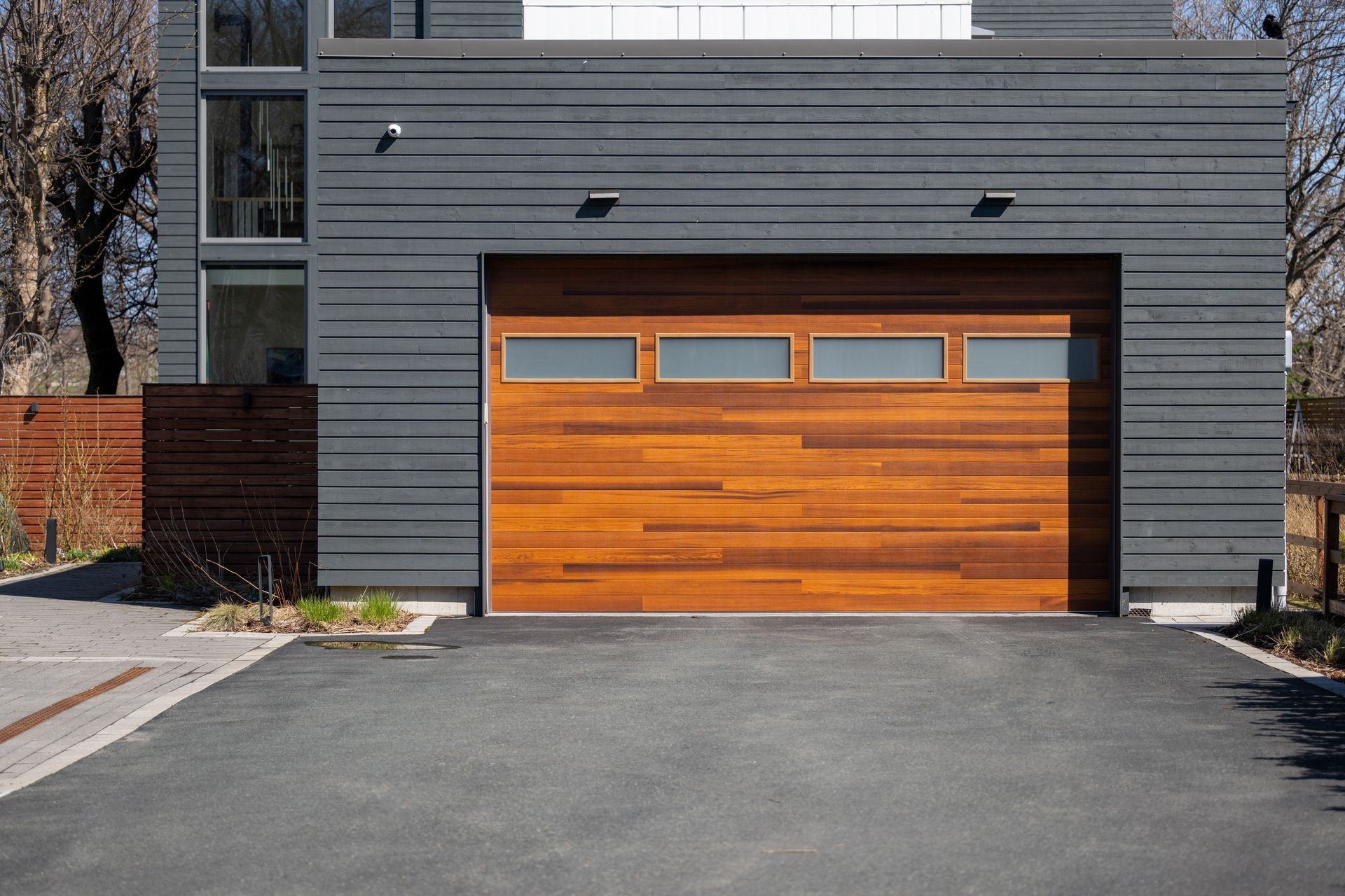 Modern house with a wooden garage door and dark gray siding; asphalt driveway.