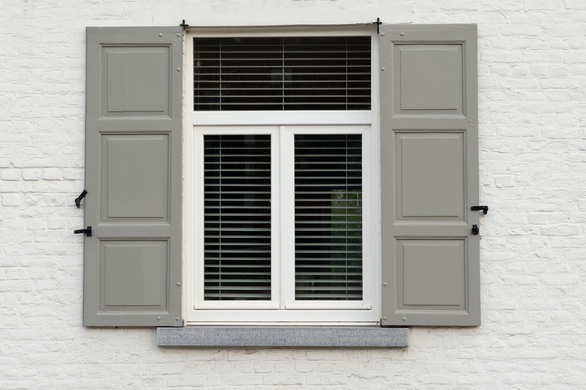 Window with open gray shutters on a white brick wall.