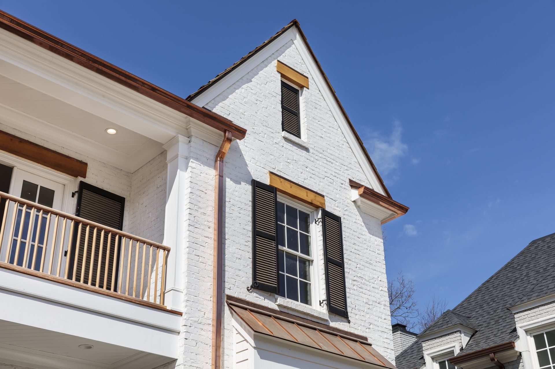 White brick house with dark shutters and copper gutters against a blue sky.