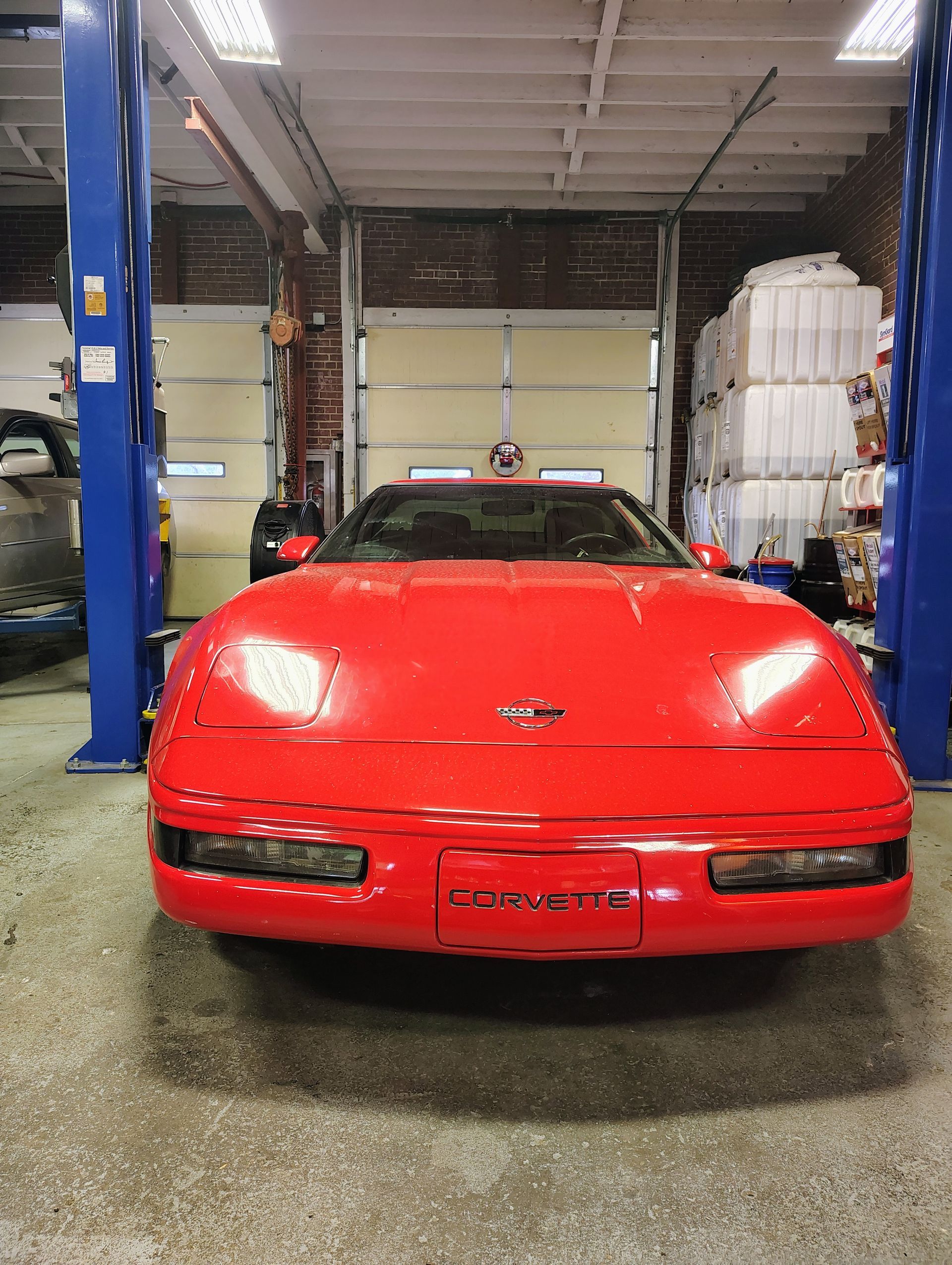 Red Corvette sports car in a garage, lit headlights, front view | MJ Auto Repair