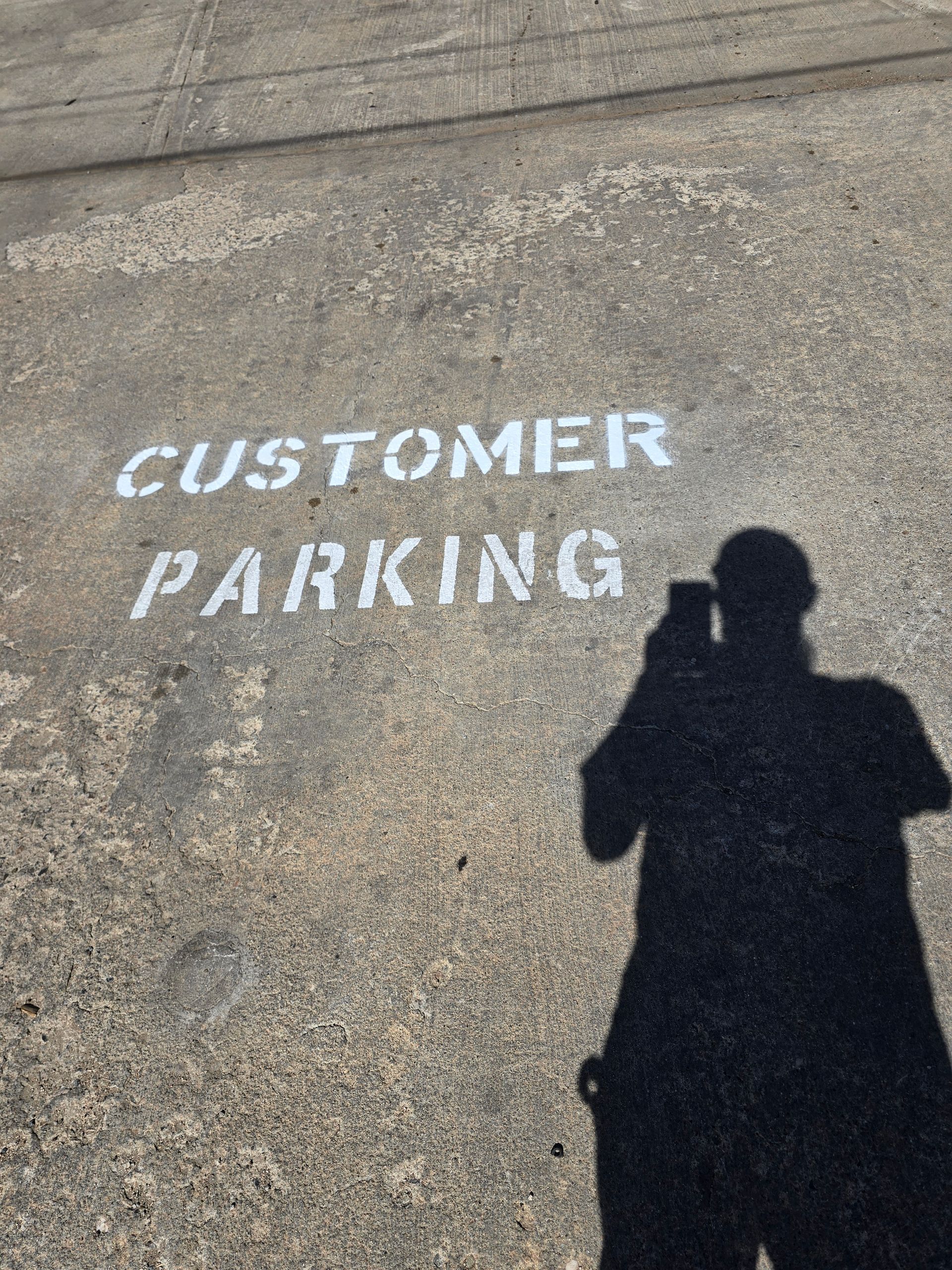 White stenciled “CUSTOMER PARKING” on asphalt, with a person’s shadow in the foreground.