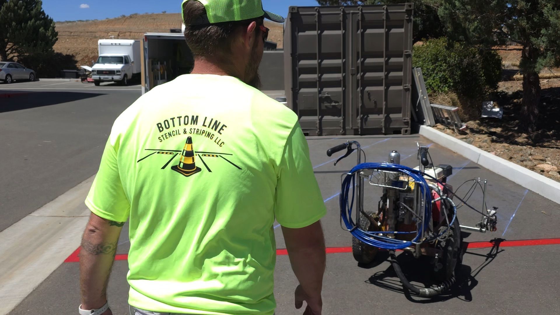 Worker in neon shirt walks toward a motorcycle on a sunny road with a trailer and truck ahead