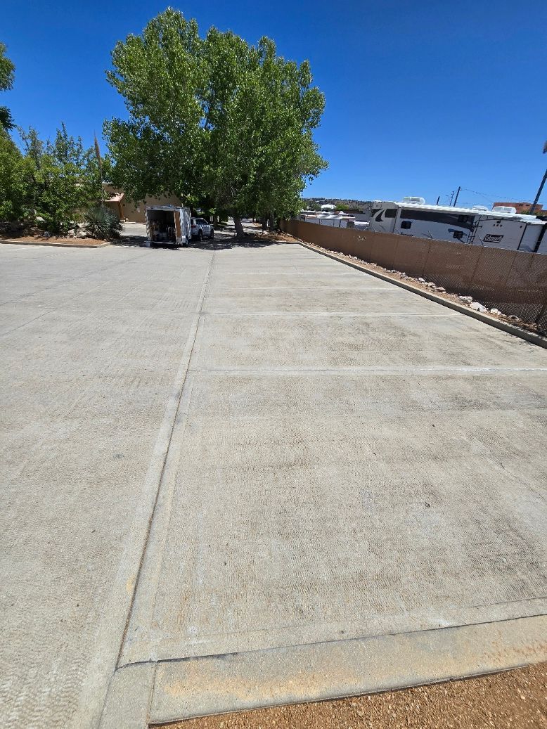 Wide concrete walkway beside a green tree and brick wall under a clear blue sky