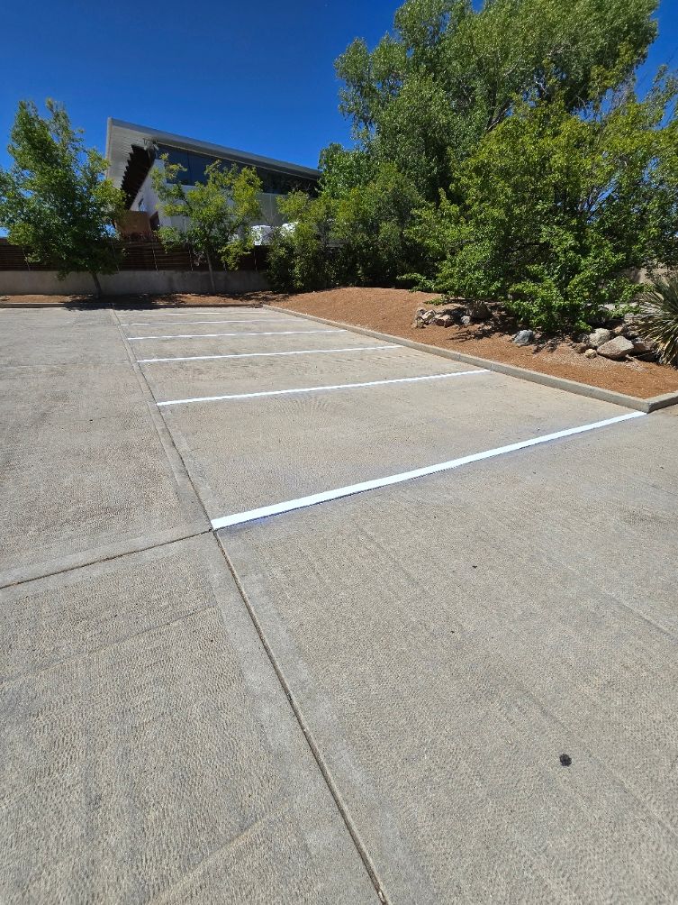Empty concrete parking area beside trees and a building on a sunny day