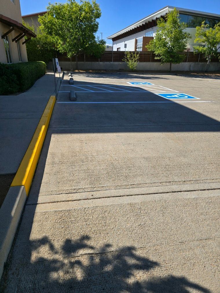 Accessible parking spaces beside a building, with yellow curb and blue pavement markings in sunlight.