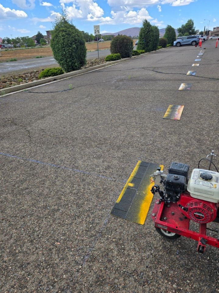 Empty parking lot with a red pavement-marking machine in the foreground and trees along the edge.