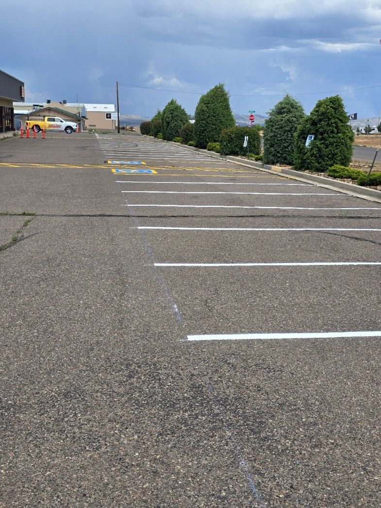 Empty parking lot with white lines, a sloped gravel surface, and cloudy sky