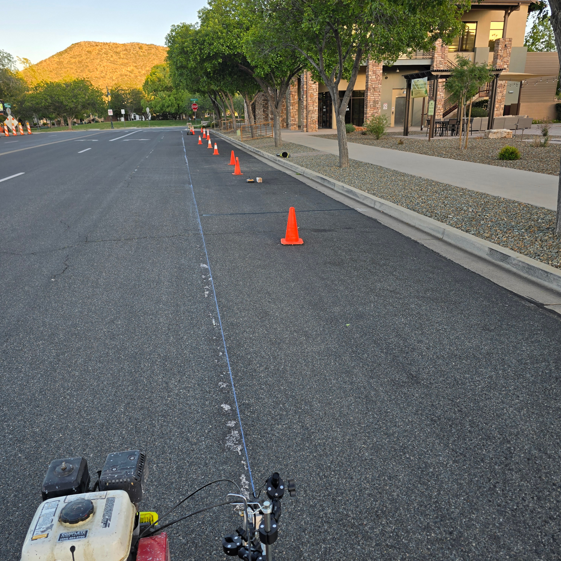 Empty street with orange cones, a curbside path, and building-lined sidewalk in warm evening light