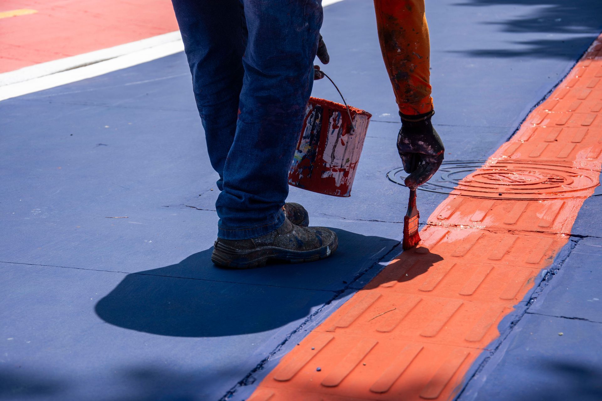 Worker painting orange lane markings on a blue sports court