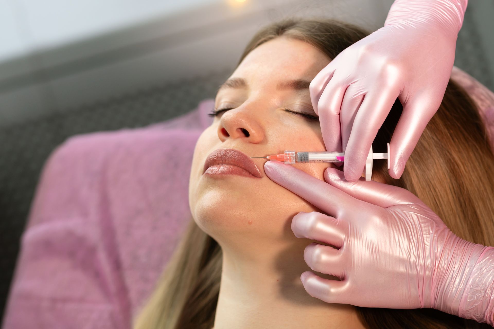 A medical professional in pink gloves performs a facial injection procedure on a patient.