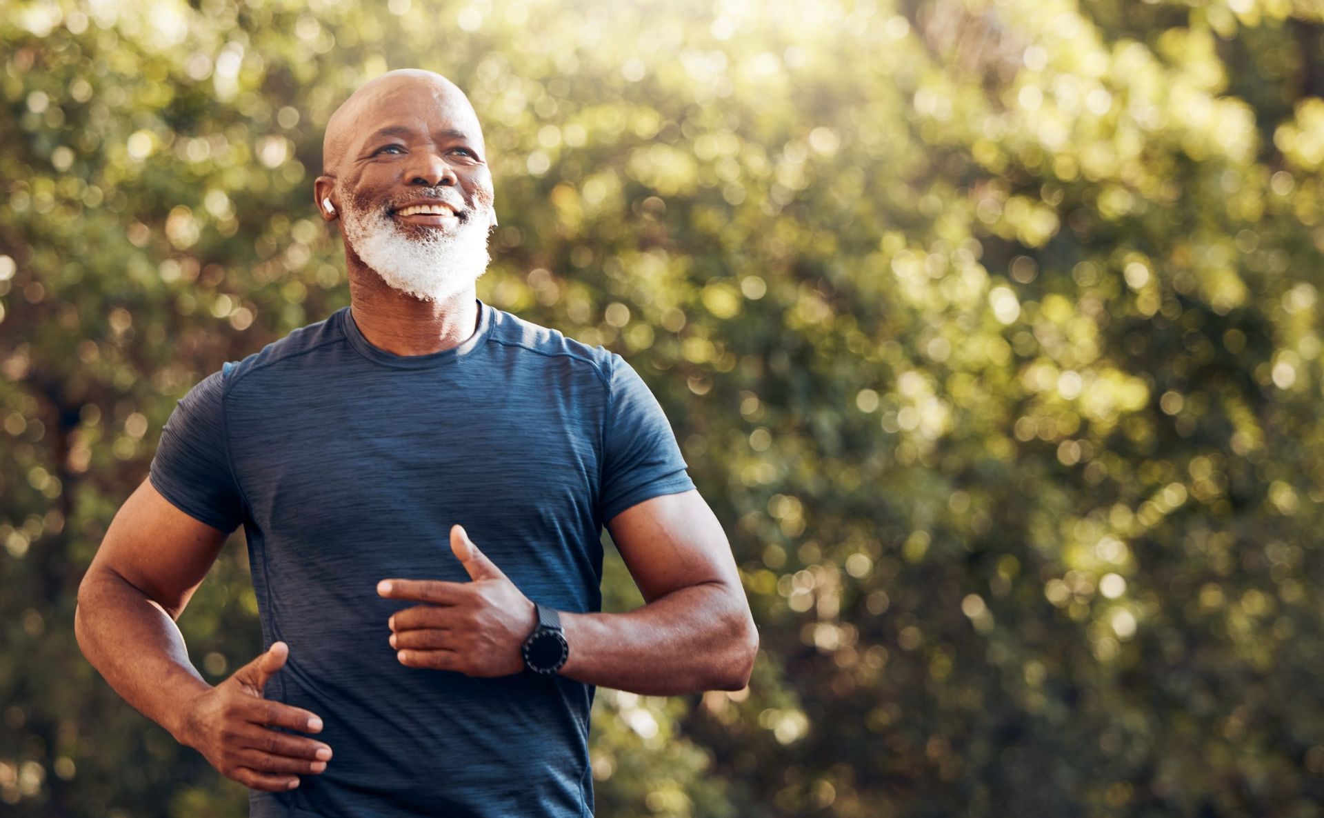Smiling man in blue shirt jogging outdoors in a sunlit park