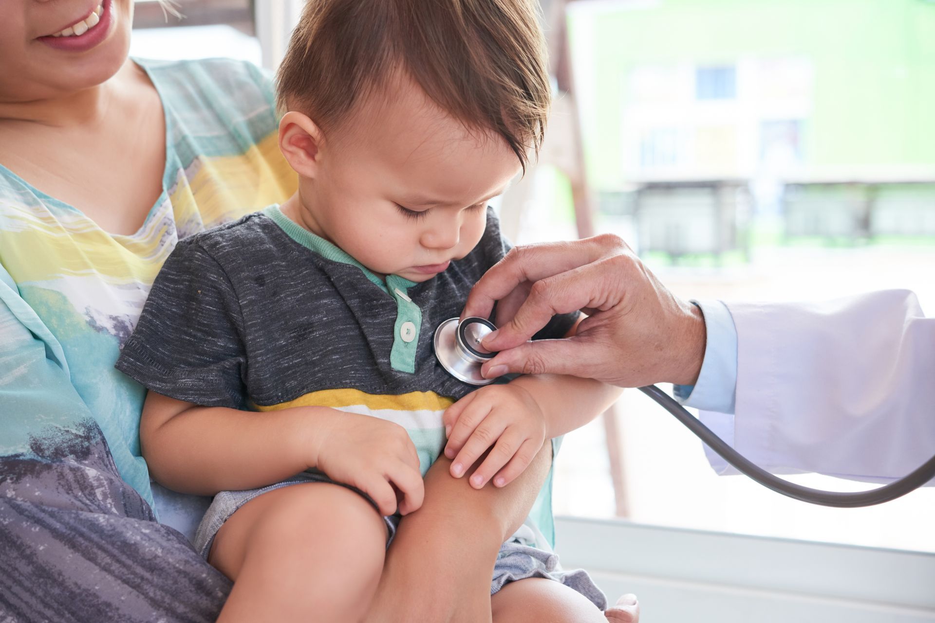 Baby being examined by a doctor while held by a caregiver, with a stethoscope on the baby's chest.