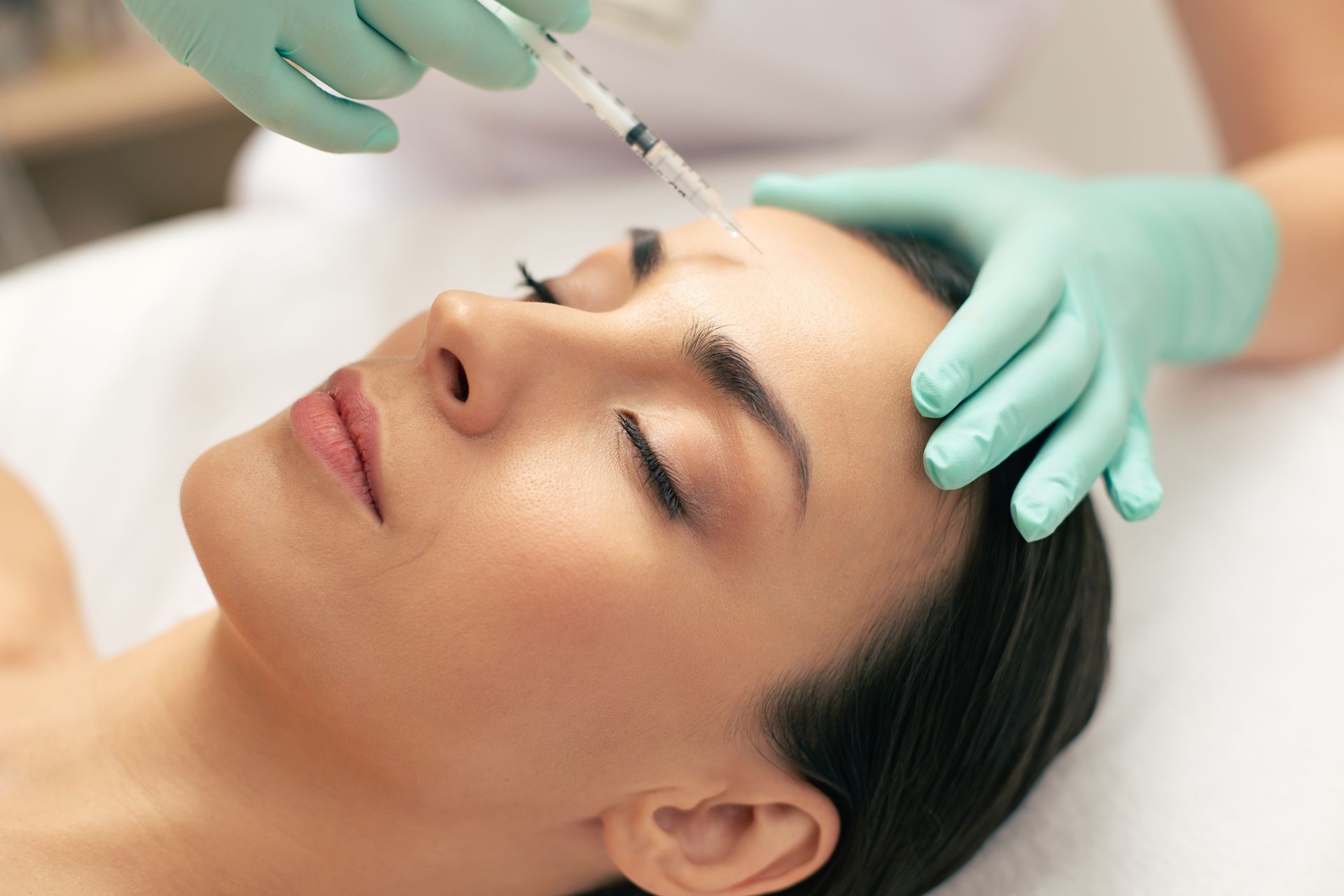 Cosmetic injection near a woman’s forehead while gloved hands steady her face