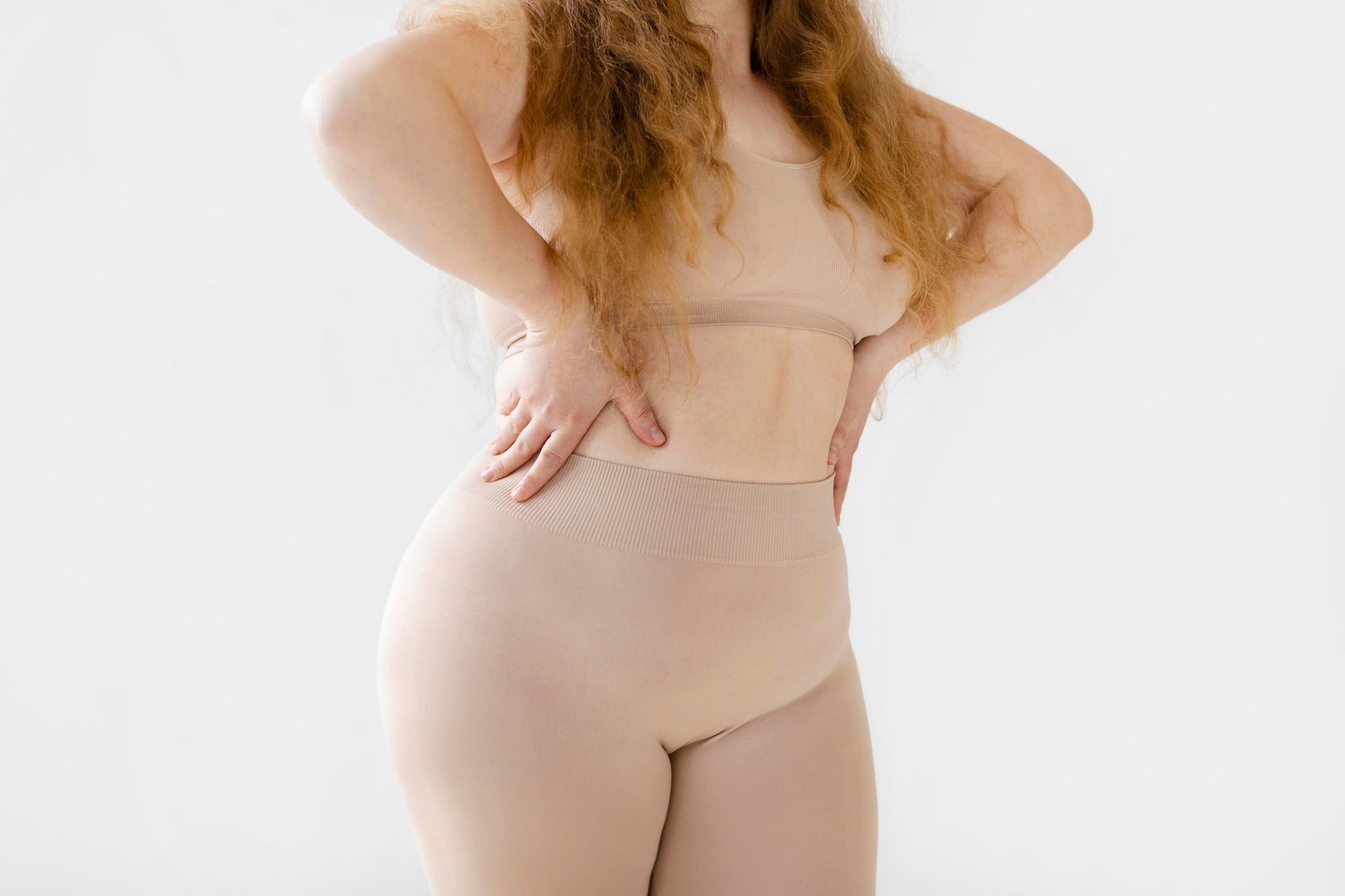 Person in beige shapewear standing with hands on hips against a white background