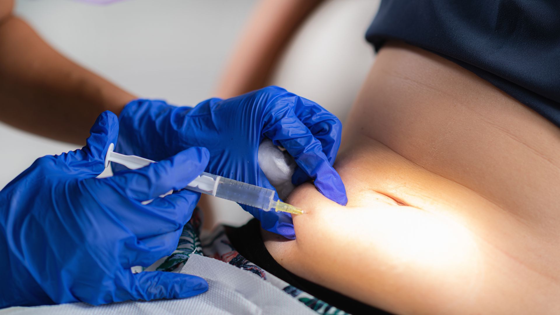 Gloved hands giving a syringe injection into a person’s upper arm