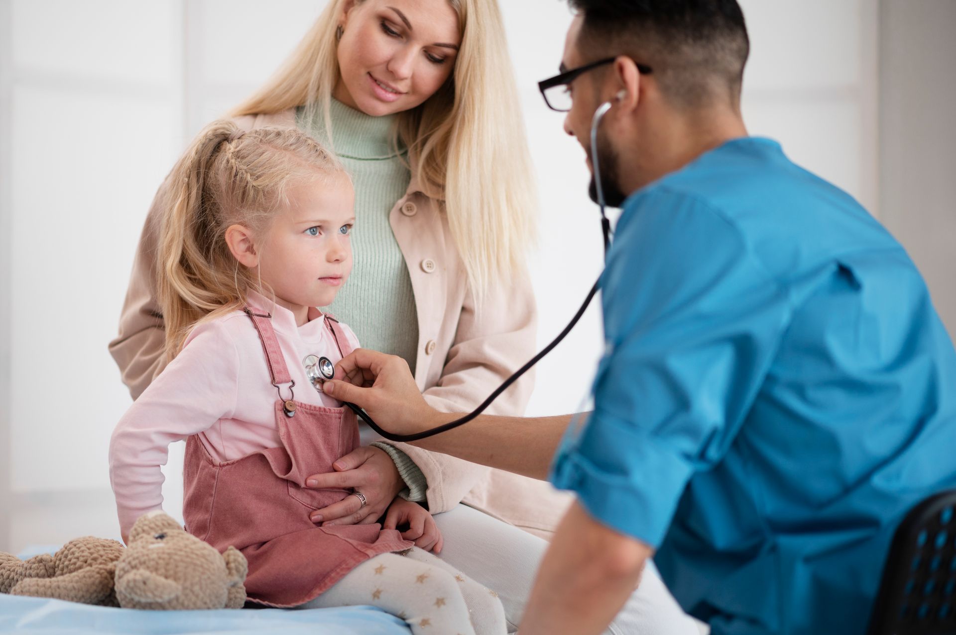 A doctor is listening to a little girl 's heart with a stethoscope.