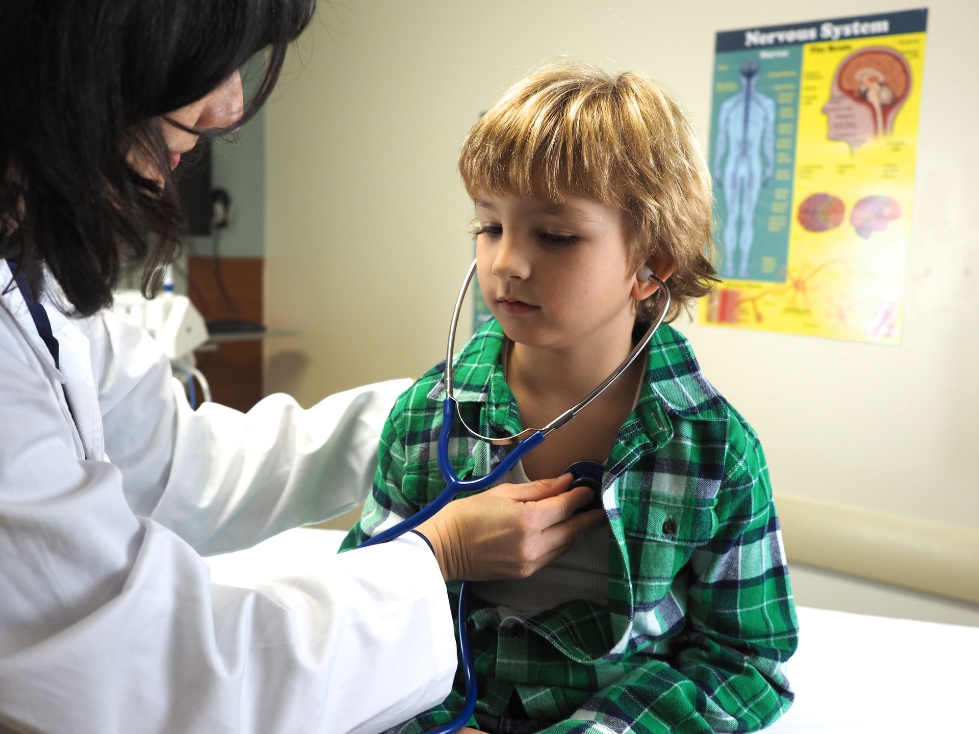 A doctor is listening to a young boy 's heart with a stethoscope.