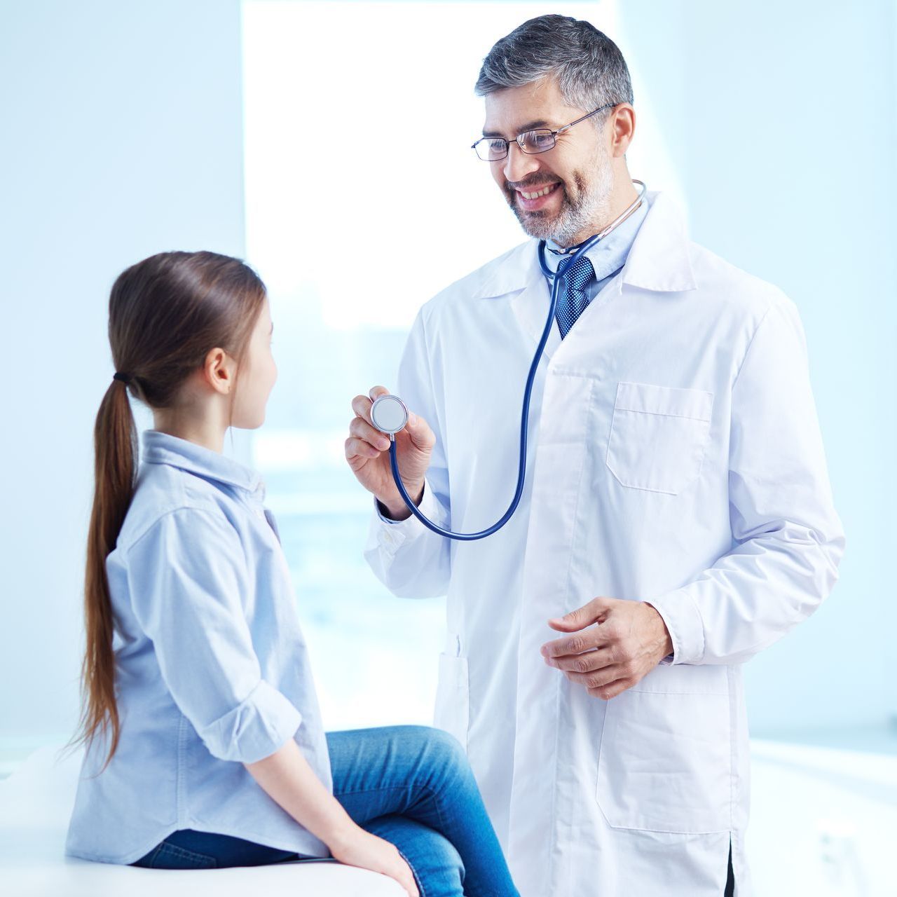 Doctor with stethoscope talking to a child patient in a bright clinic room