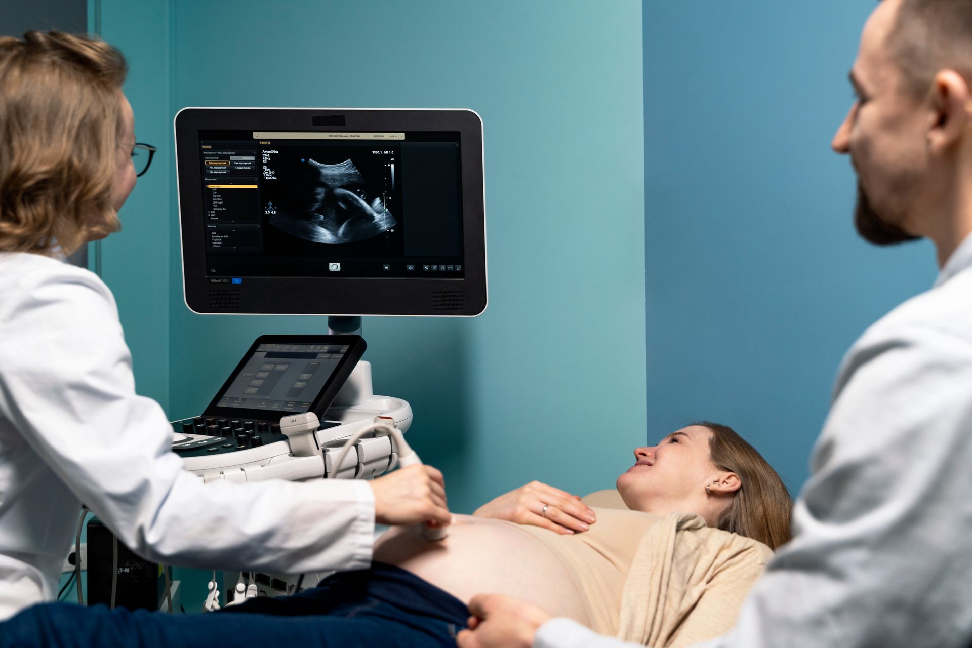 Ultrasound exam with clinician, patient on exam table, and monitor showing scan in a medical room