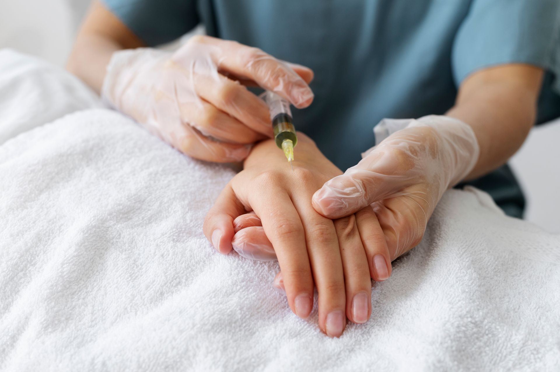 Gloved hands inject medication into a patient’s hand on a white towel