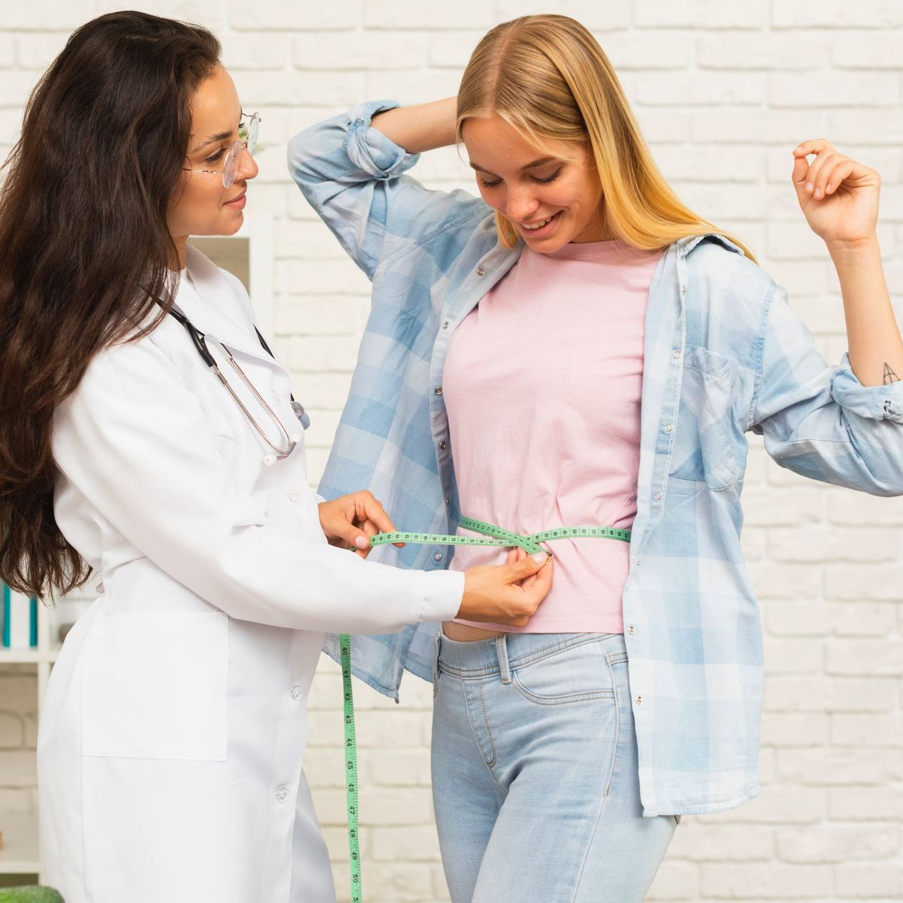 Doctor measures a woman's waist with a tape measure in a bright clinic.