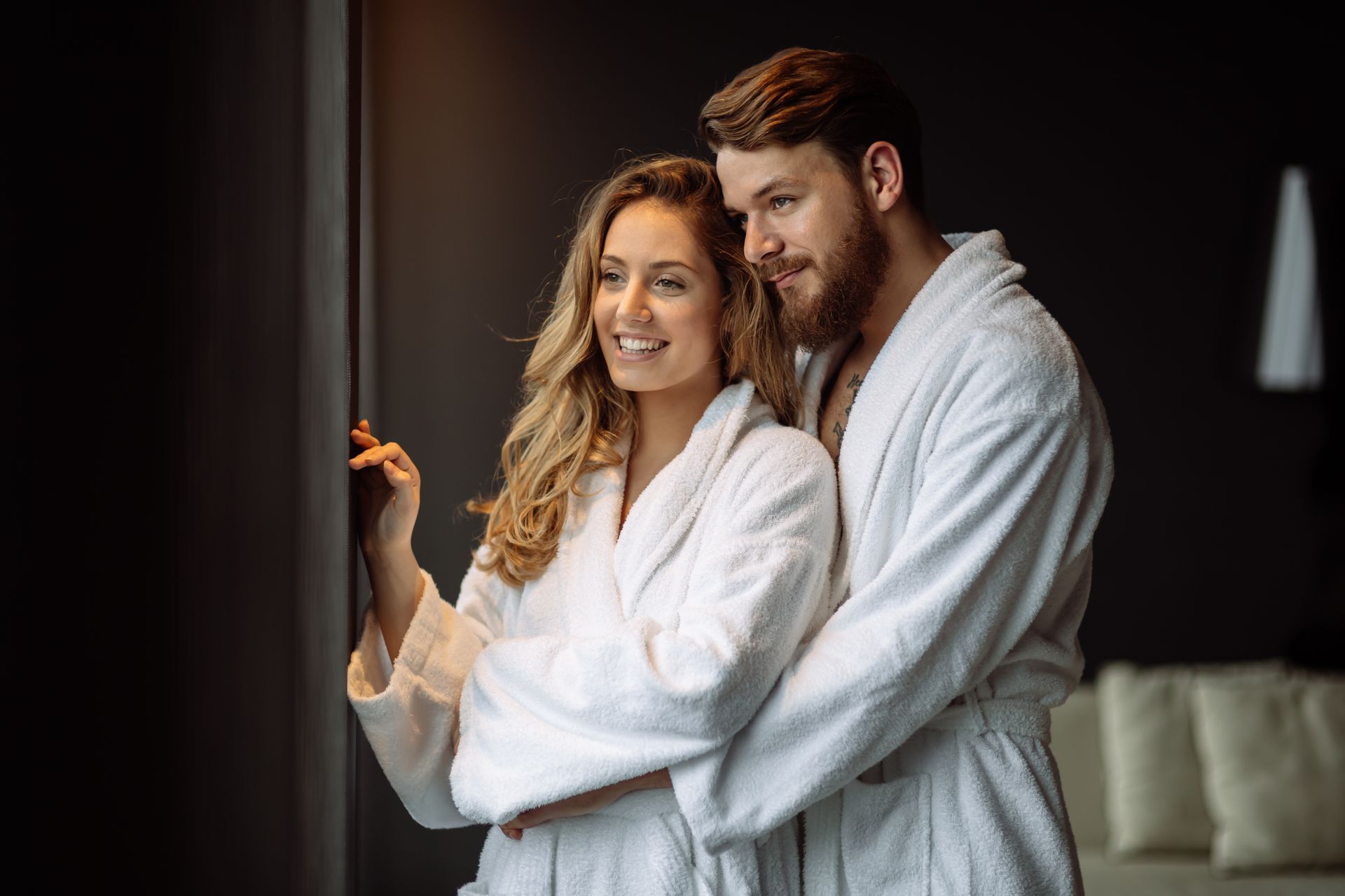 Couple in white robes embracing and smiling in a dimly lit bedroom