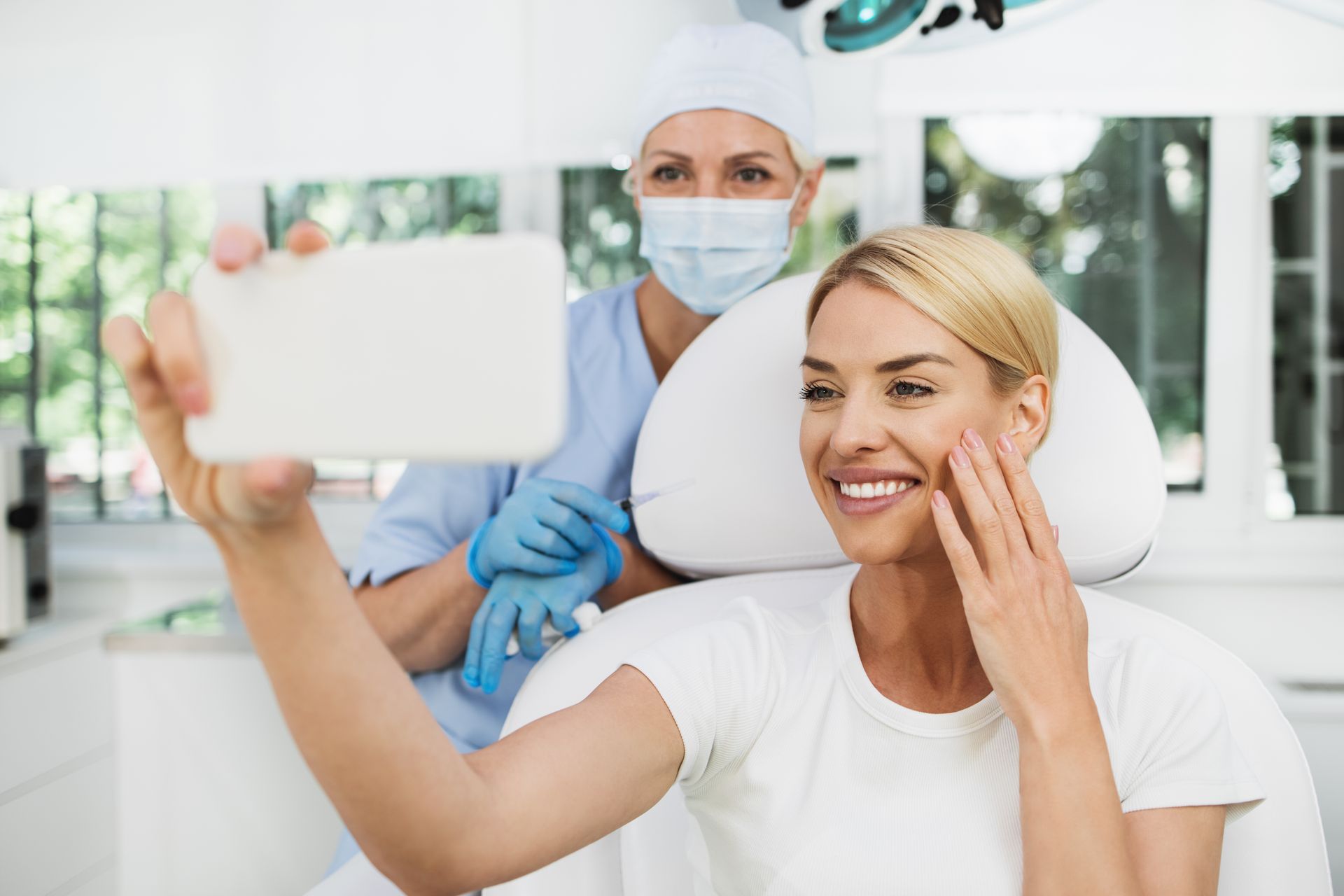 Patient taking a selfie while dentist in mask and gloves smiles in a bright dental office