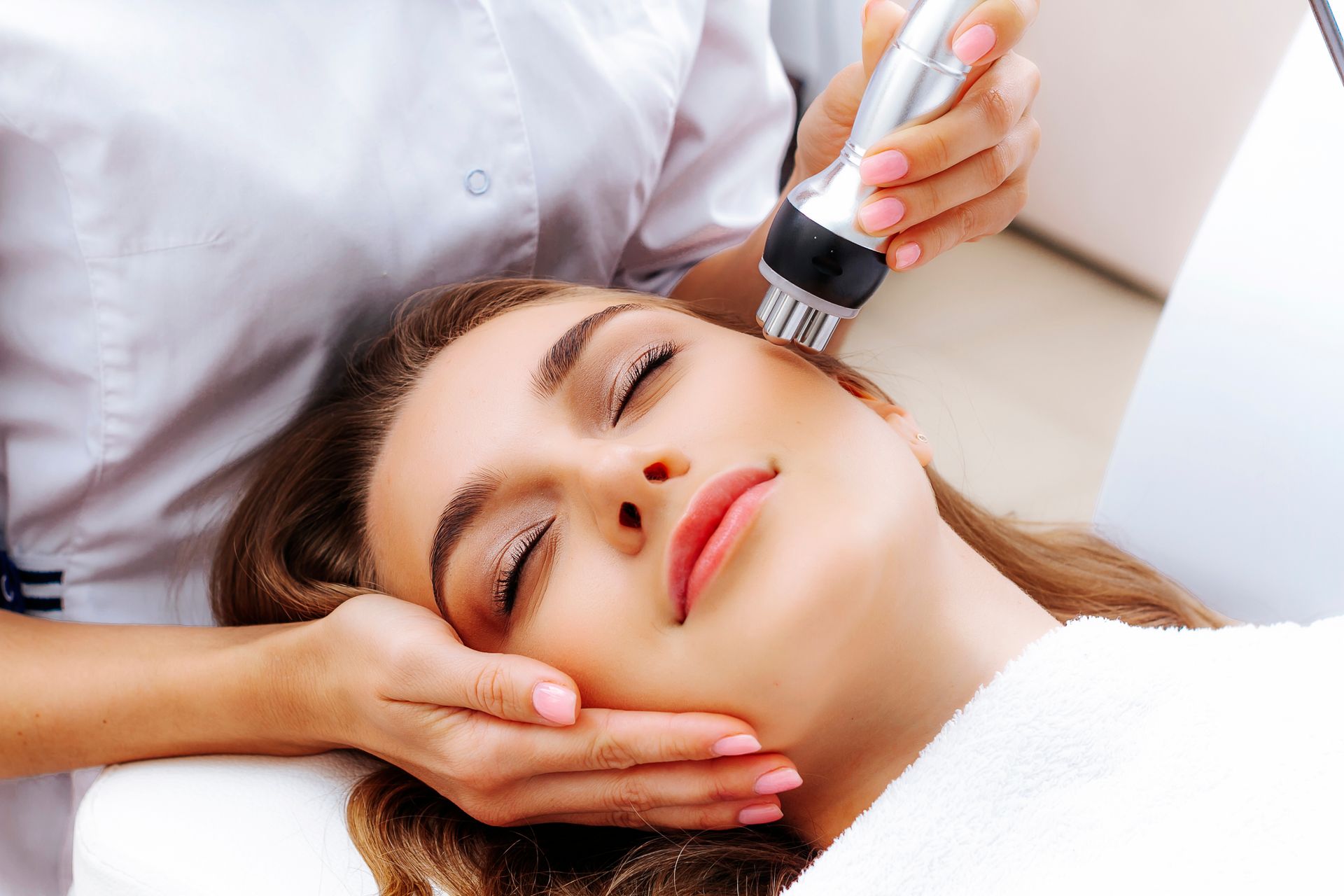 A facial treatment in progress, with a therapist applying a device to a woman’s face