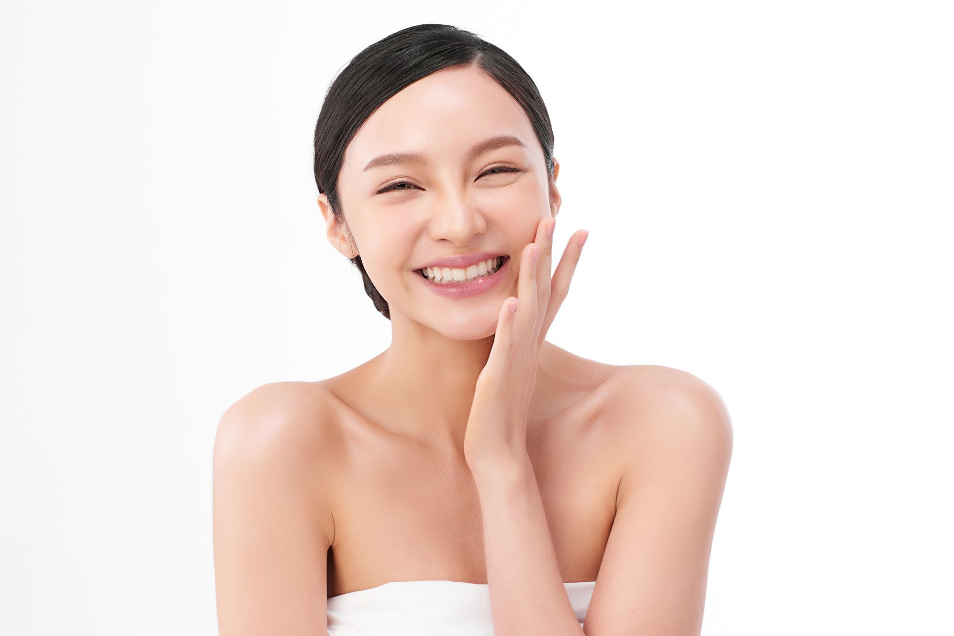 Smiling woman with a towel on her head, touching her cheek against a white background