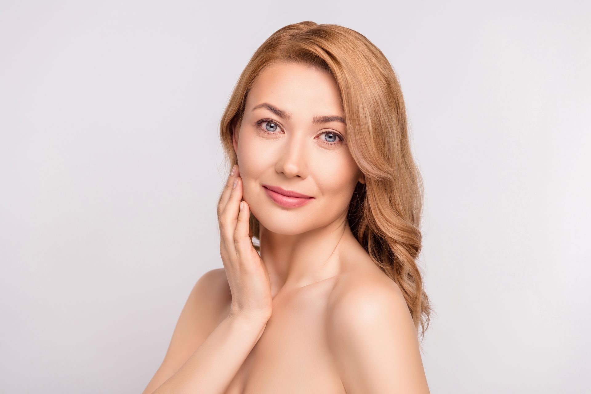 Portrait of a smiling person with a hand on their cheek against a light background